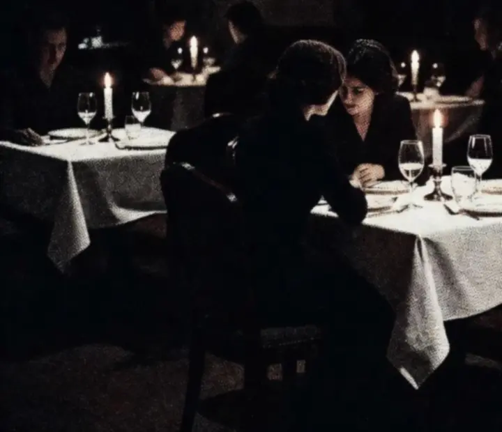 Salle de restaurant en noir et blanc, tables serrées, bougies et ambiance cinématographique.